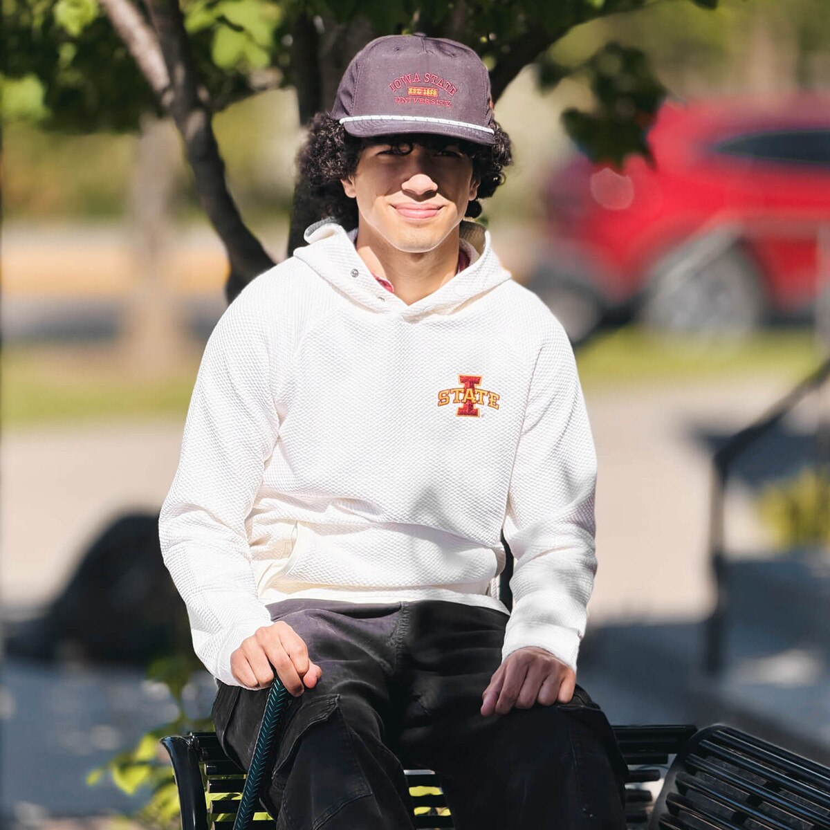 Lifestyle of student wearing Swannies I-State White Camden Hooded Sweatshirt on a bench with a Swannies hat
